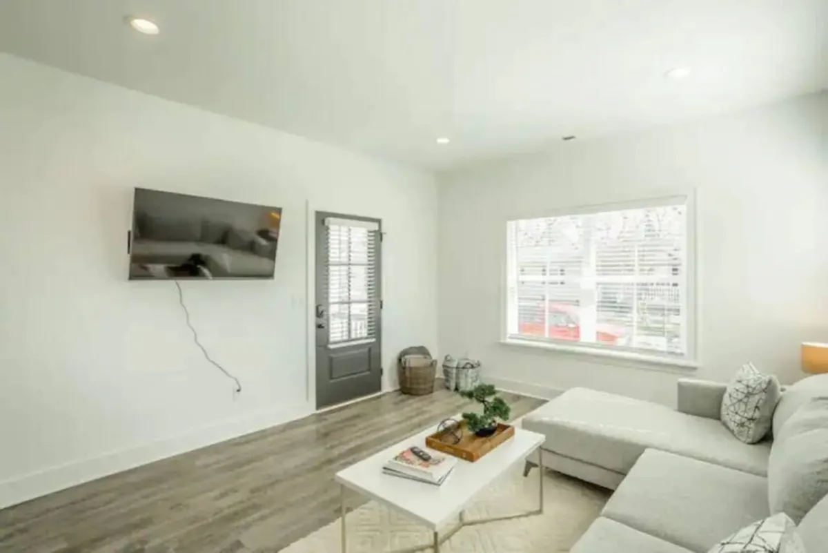A cozy living area with a comfortable sofa facing a TV, a coffee table, a doorway, and a window letting in natural light. The setting is inviting, ideal for relaxing, socializing, or watching TV after an eventful evening out.