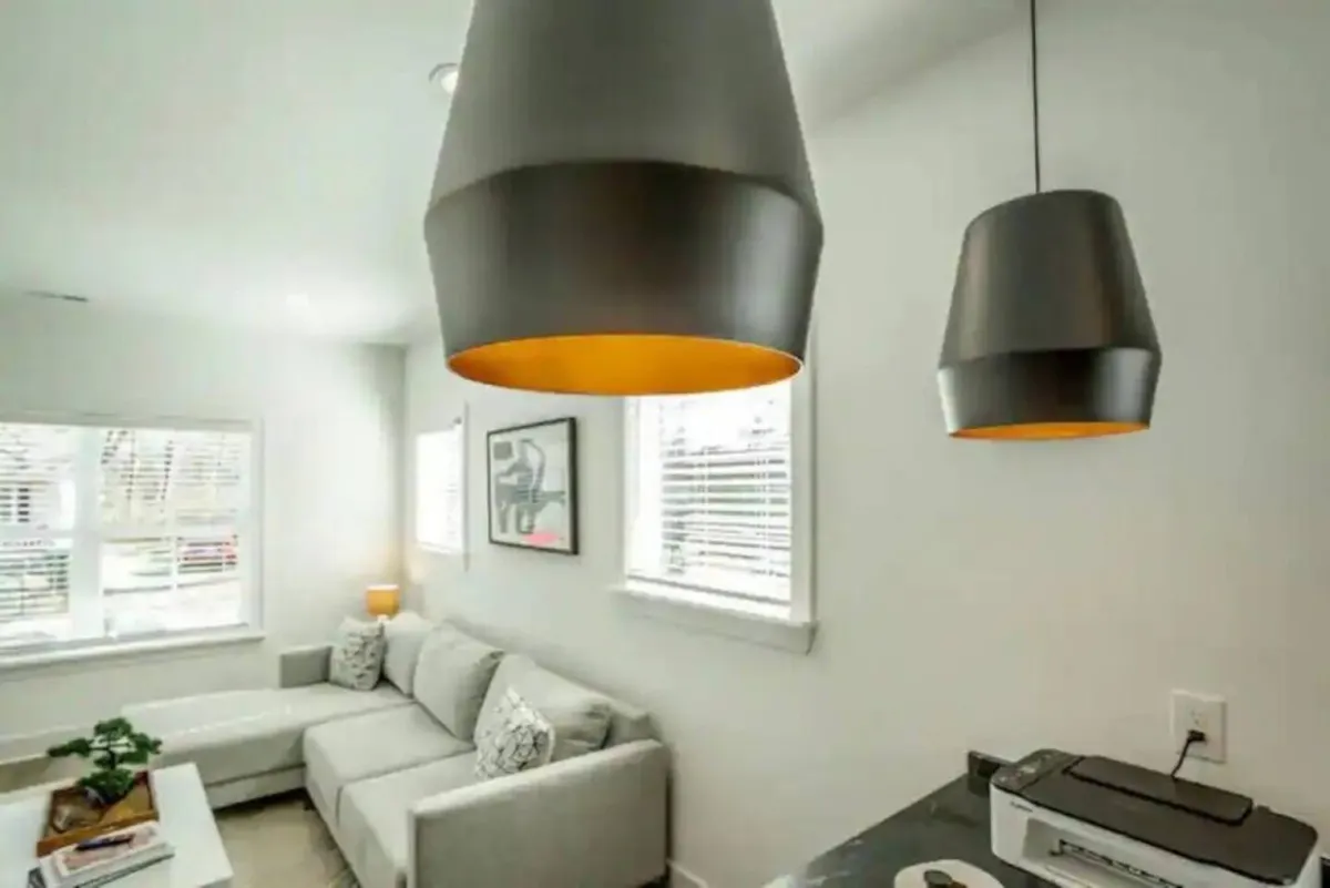 A cozy corner of the living room with a soft sofa, eye-catching hanging light fixtures, and vibrant artwork on the wall. The space is designed for relaxing, reading, or enjoying lively discussions in a contemporary environment.