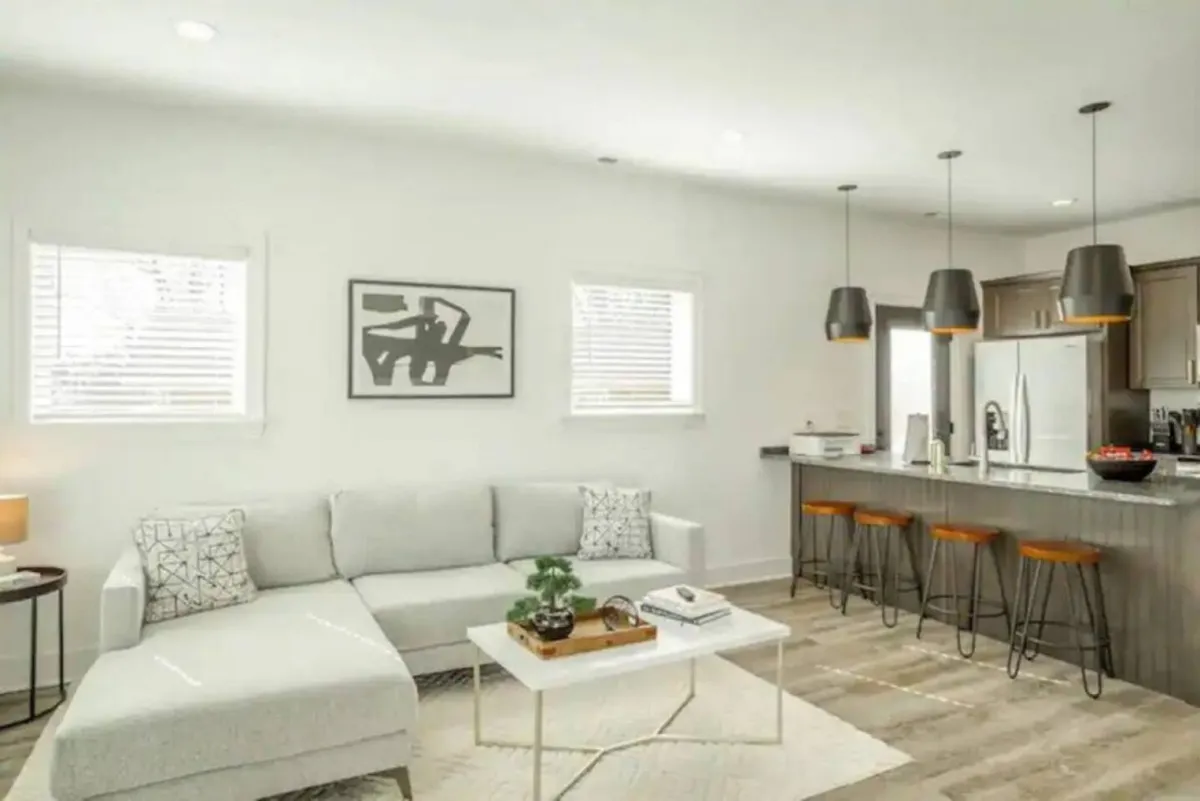 A contemporary living area featuring a spacious sectional sofa, a stylish kitchen island, and modern artwork on the wall. The open-concept design provides a welcoming transition between the social spaces, hinting at both comfort and convenience for families gathering together after a day of exploring Chattanooga.