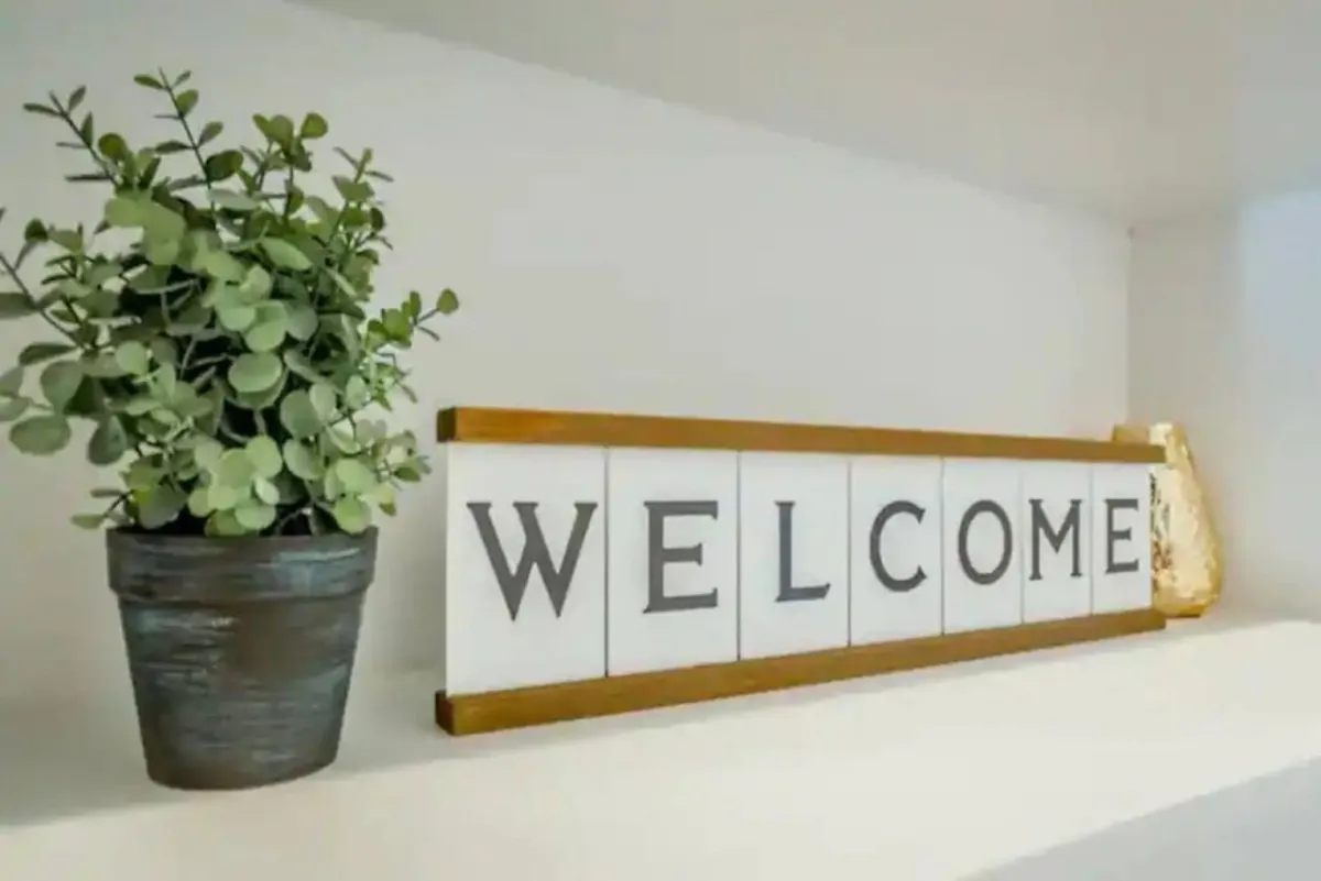 An inviting entryway featuring a welcome sign and a lush potted plant. The space radiates hospitality and the first touchpoint for guests, setting a comforting, friendly tone as one enters the home.
