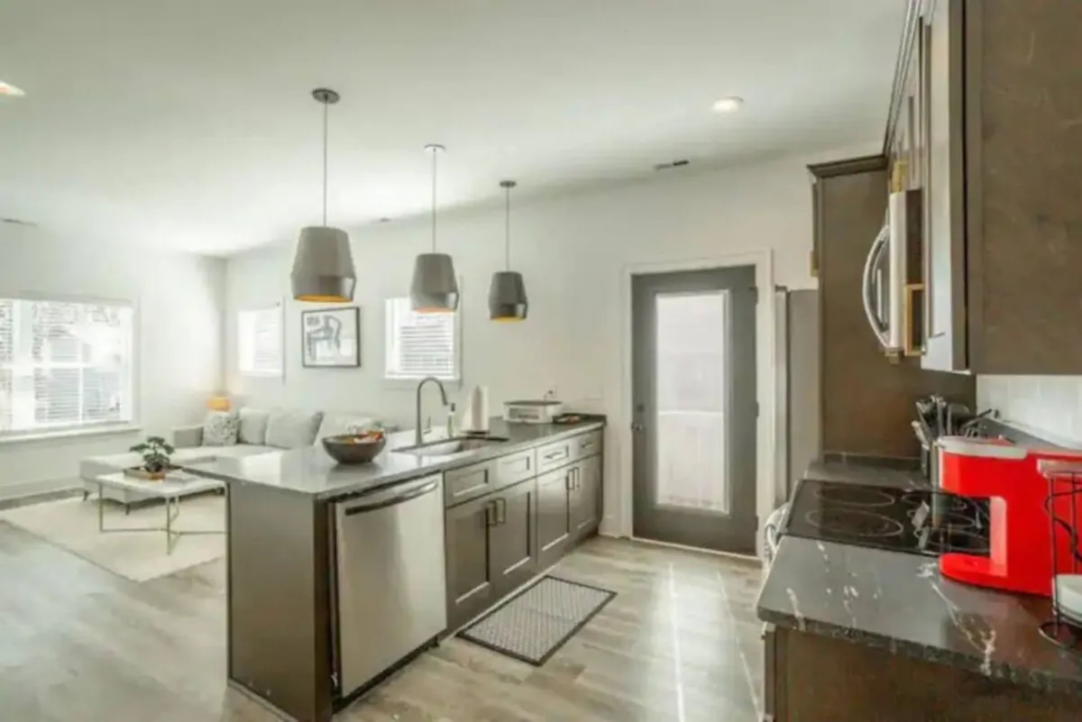 A warm, inviting kitchen scene focused on an island countertop with pendant lighting overhead and adjacent seating, suggesting space for cooking, entertaining, and gathering as a group.