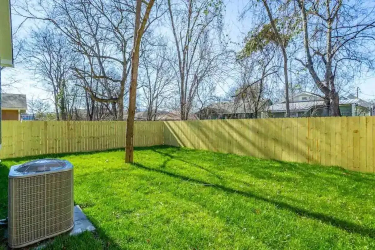 A peaceful backyard view featuring bright green grass, a sturdy wooden fence, and several trees. The space feels open and safe for both pets and people alike, ideal for morning coffee, sunset views, or leisurely outdoor activities.