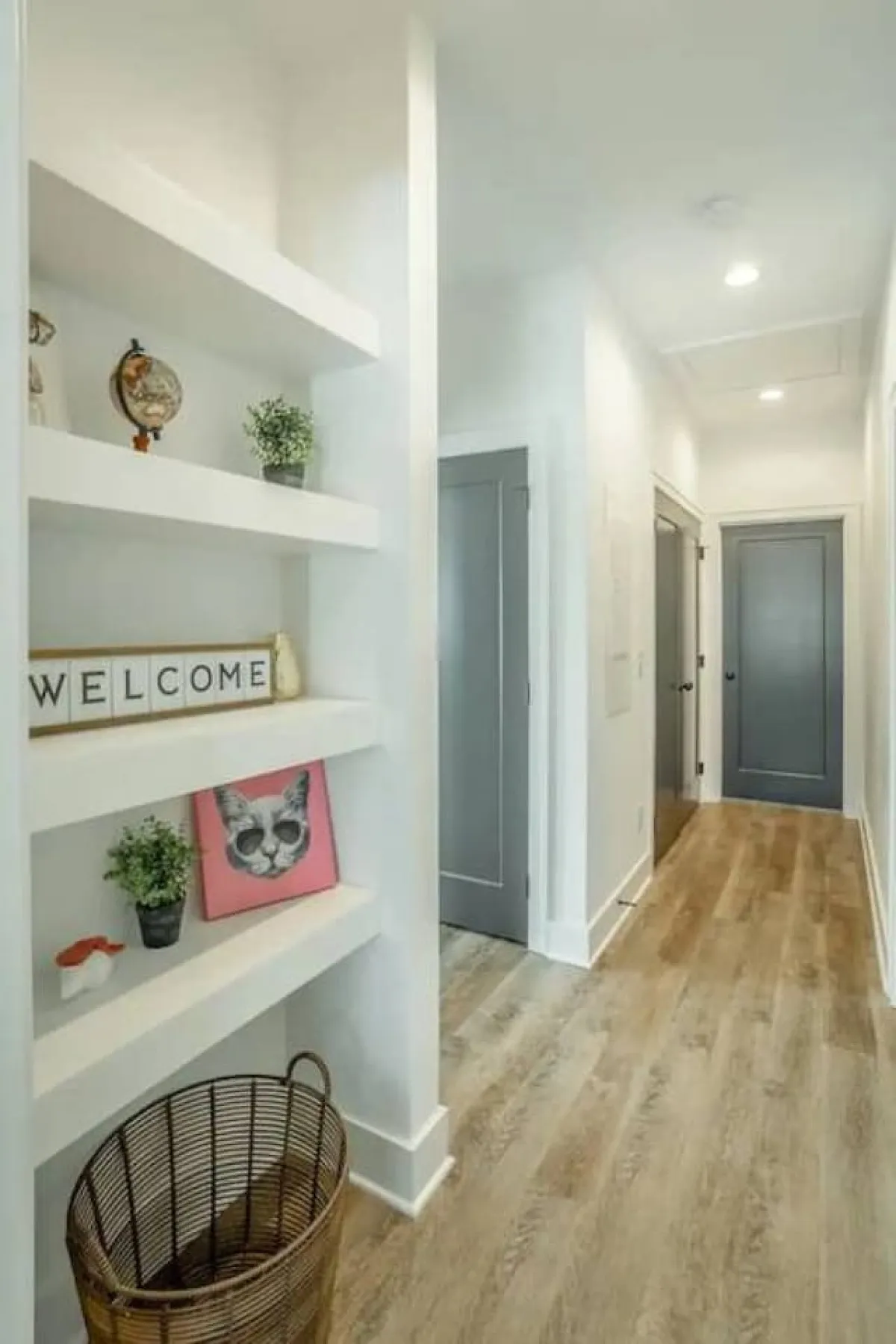 A cozy set of shelves decorated with a welcoming sign and playful cat artwork, complemented by neatly organized baskets and other personal touches. The décor injects character and subtly signals a pet-friendly, cared-for environment.