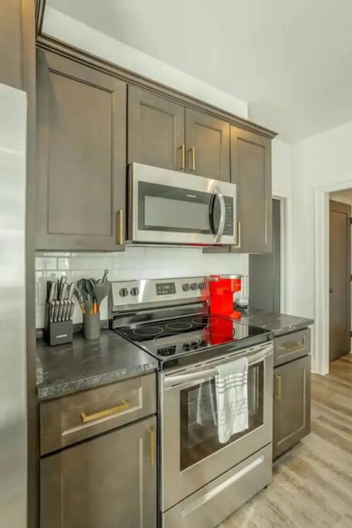 A welcoming, contemporary kitchen showcasing stainless steel appliances, dark cabinetry, a granite countertop, and a pop of color from a red kettle. The space is designed for both cooking and entertaining, with clear sightlines and plenty of prep space.