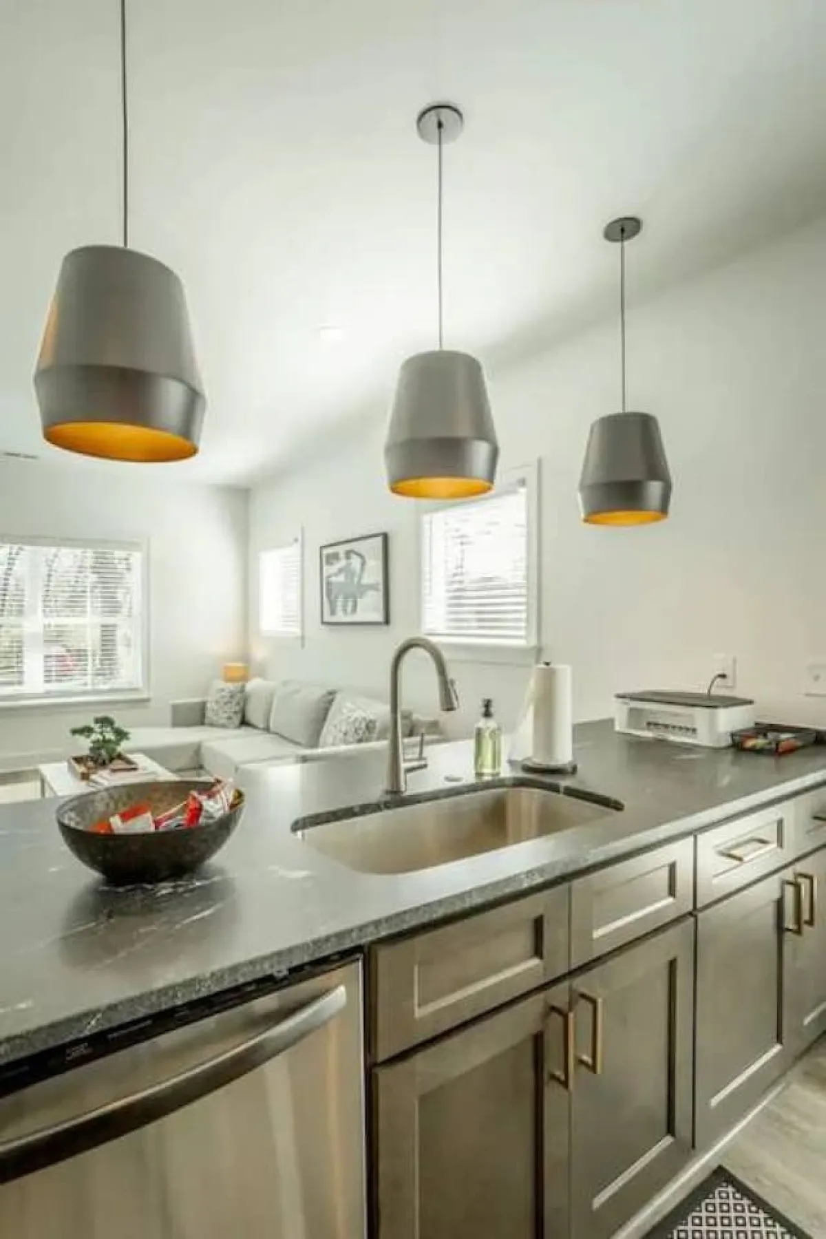 A modern kitchen with pendant lights illuminating the sleek countertop and sink, while comfortable seating in the living area is visible in the background. This inviting space suggests easy entertaining and unwinding, reinforcing the idea of a safe, private retreat at the end of a busy day.
