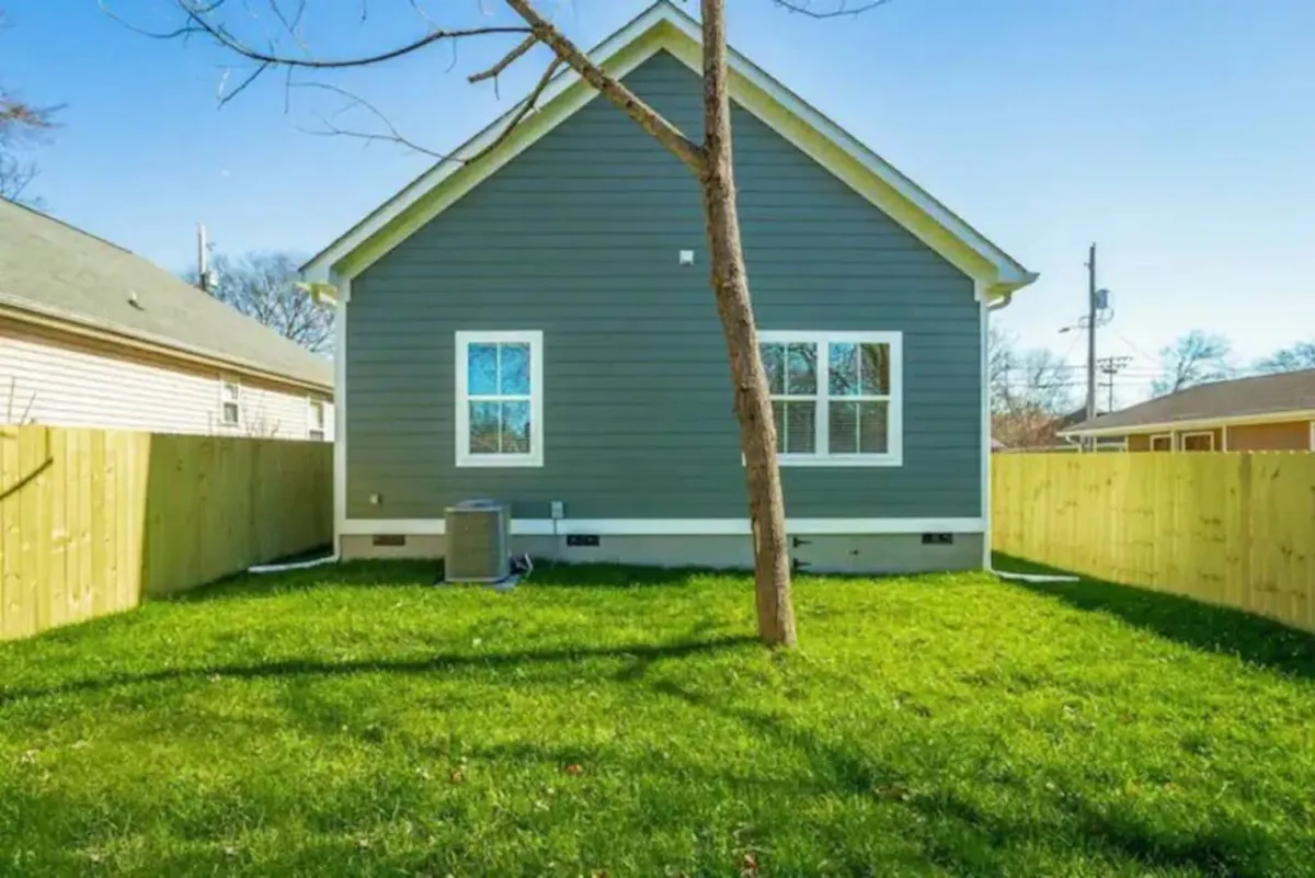 This image features a tranquil scene of a lush, green fenced yard with a tree and the exterior of the house visible. The grassy area is well-suited for pets to play safely outdoors. The setting hints at activities like outdoor gatherings and relaxing on the patio, all within a secure environment perfect for four-legged family members.